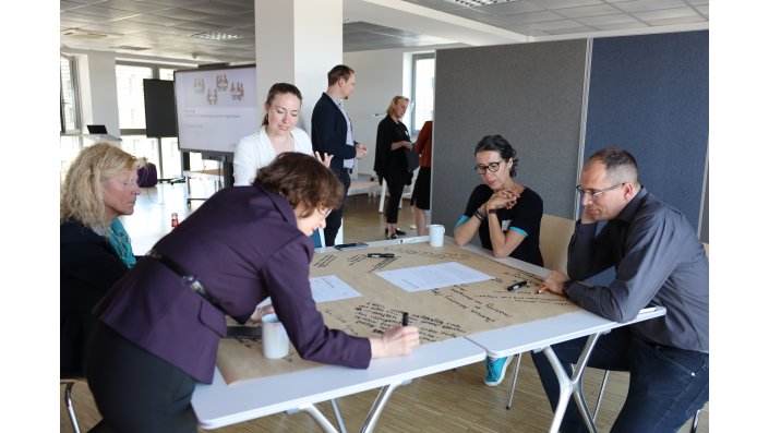 Eine Personengruppe arbeitet an einem der World-Café-Tische.