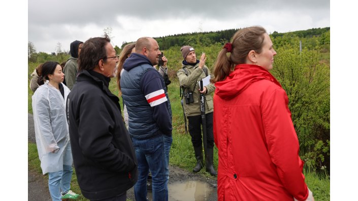 Dr. Dominik Schüßler steht mit der Gruppe am Wegesrand und zeigt in eine Richtung.