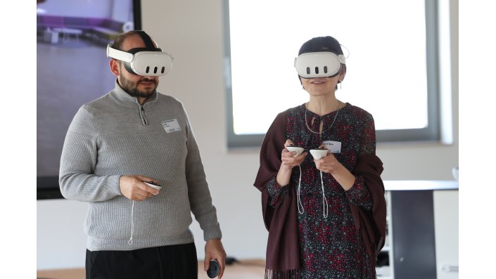 Eine Frau mit VR-Brille lächelt. Neben ihr steht Workshopleiter Muhammet Celik für Fragen bereit.