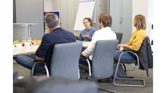 Die Teilnehmenden sitzen um einen großen Tisch und lauschen Julia Gerbers Ausführungen.