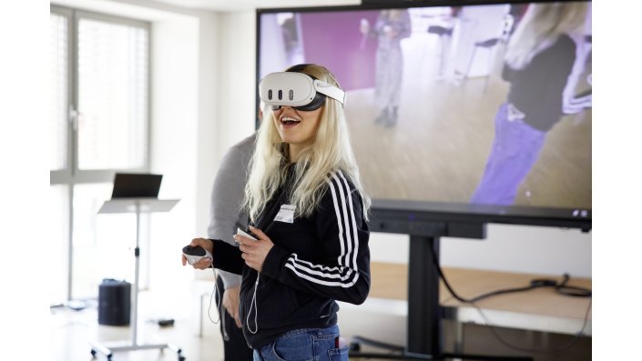 Eine junge Frau mit VR-Brille lacht beglückt.