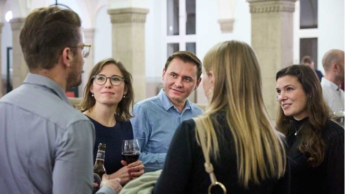 Teilnehmende der Abschlussfeier des Masterstudiengangs Versicherungsrecht LL.M. an der TH Köln im Gespräch beim feierlichen Ausklang im Foyer des historischen Gebäudes an der Claudiusstraße 1.