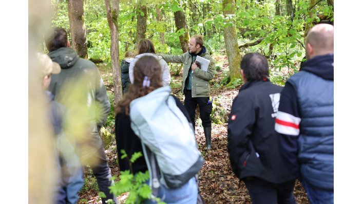 Die Gruppe lauscht im Wald den Ausführungen von Dr. Dominik Schüßler.