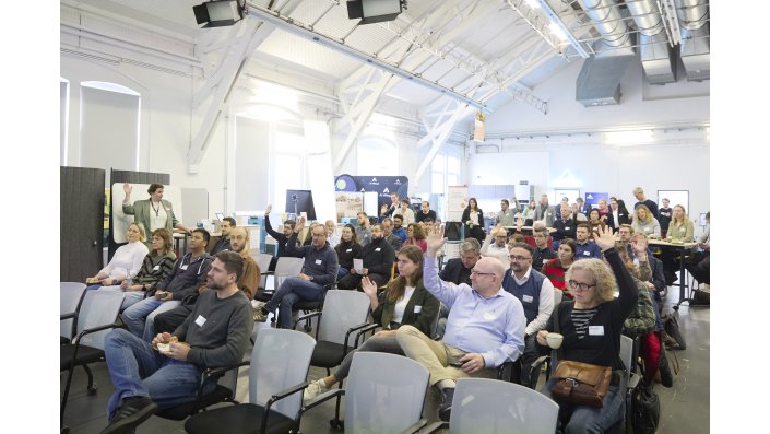 Mehrere Personen im Publikum heben die Hand.