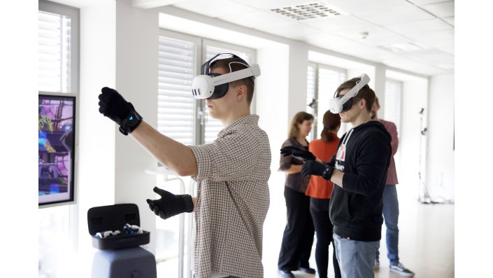 Ein junger Mann trägt VR-Brille und bHaptics-Handschuhe. Dabei macht er mit der einen Hand eine Faust.