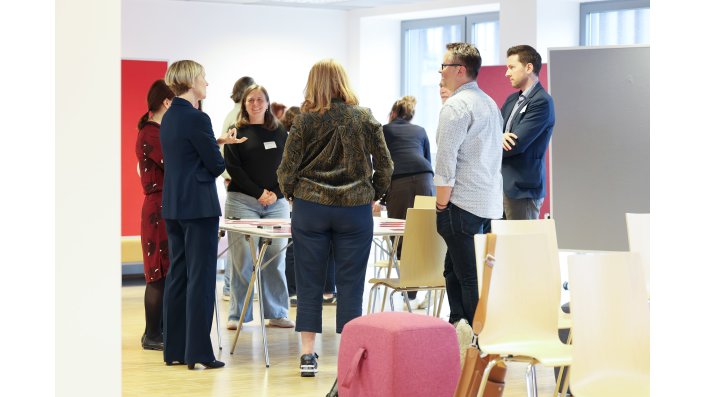 Eine Gruppe von sechs Personen steht um einen mit Ausdrucken belegten Tisch und diskutiert dazu.