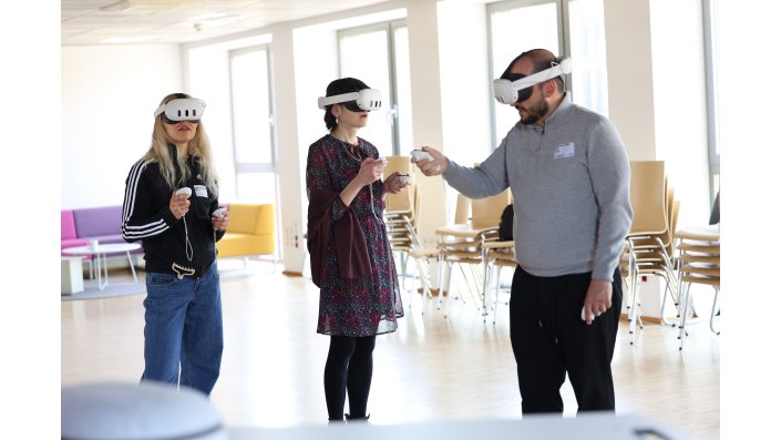 Zwei Frauen mit VR-Brillen werden durch Workshopleiter Muhammet Celik, ebenfalls mit VR-Brille, in VR eingewiesen.