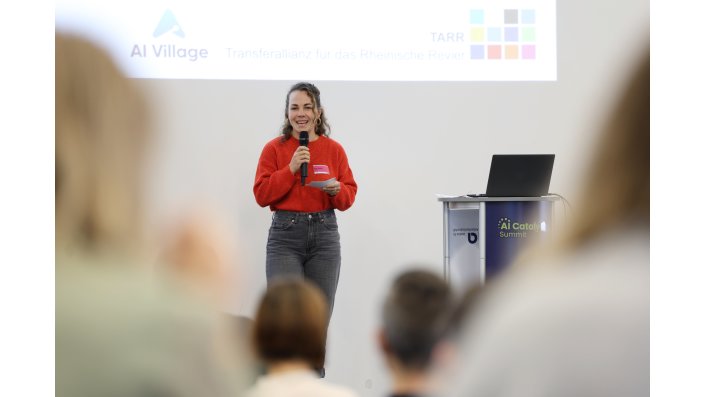 Die Moderatorin der Veranstaltung steht lachend auf der Bühne.