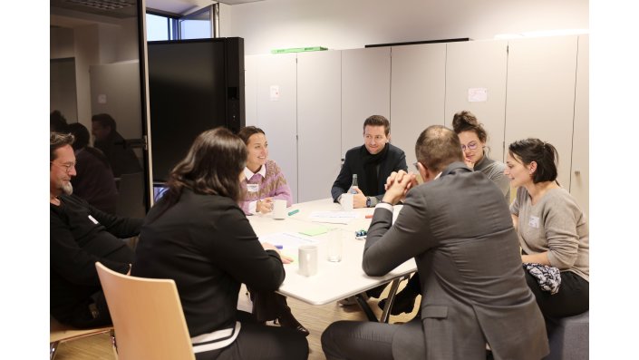 Eine große Gruppe sitzt diskutierend um einen Tisch.