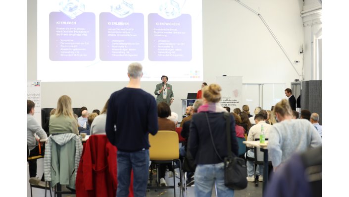 Zahlreiche Besucher blicken in Richtung einer Bühne, wo sich das AI Village vorstellt.