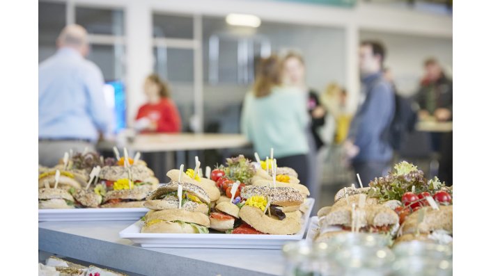 Ein buntes Buffet vor dem Hintergrund von Personengruppen im Gespräch.